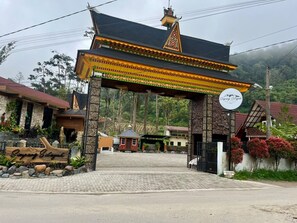 A traditional gate with a sign, a paved entrance, and a mountain backdrop.