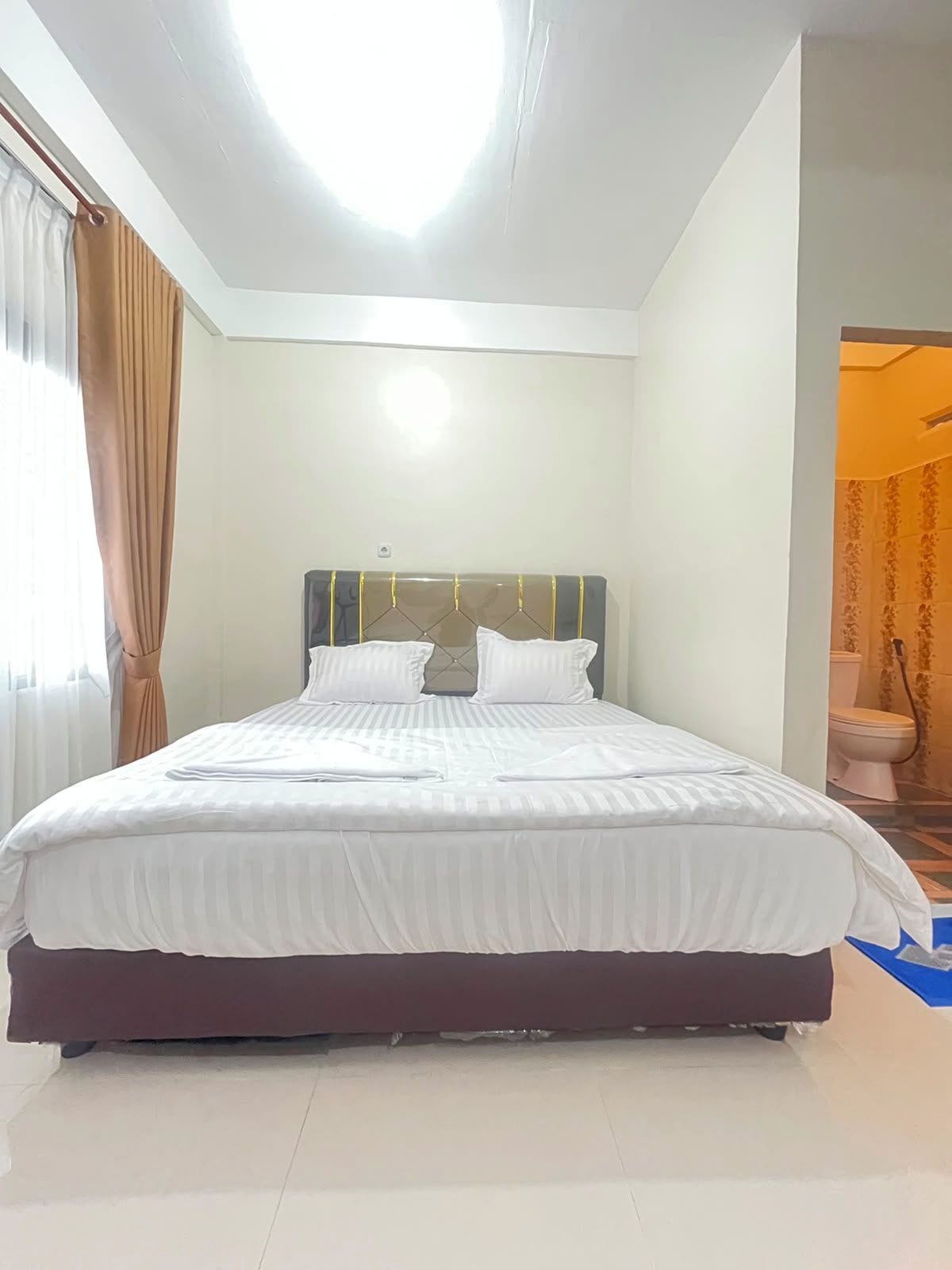 A neatly made bed in a hotel room with a headboard, a visible power outlet, and a bathroom door in the background.