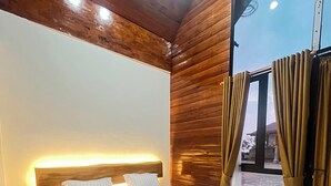 Quarto com cabeceira de madeira, cama com roupa de cama branca e uma janela grande com cortinas.