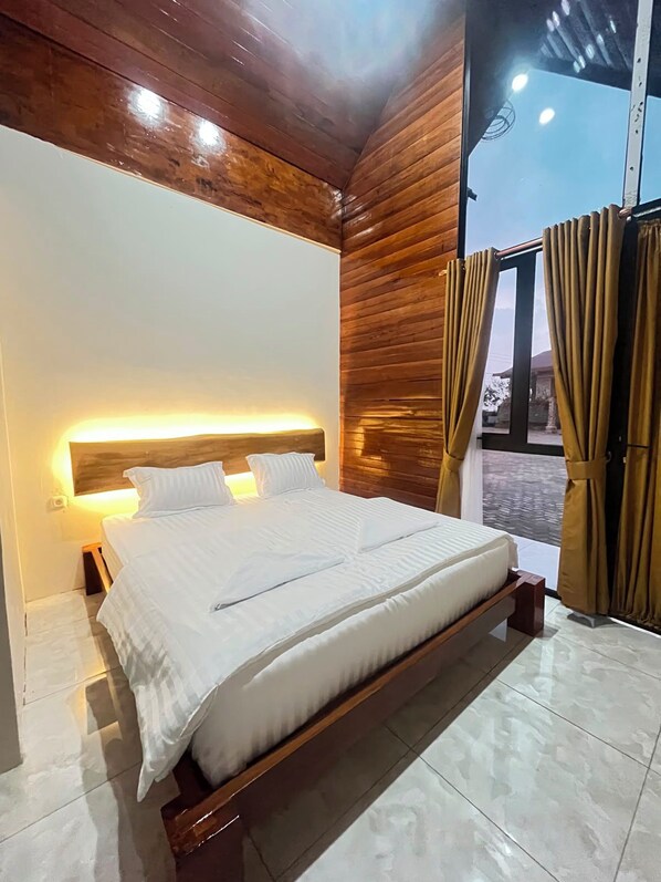 A bedroom with a wooden headboard, a bed with white bedding, and a large window with curtains.
