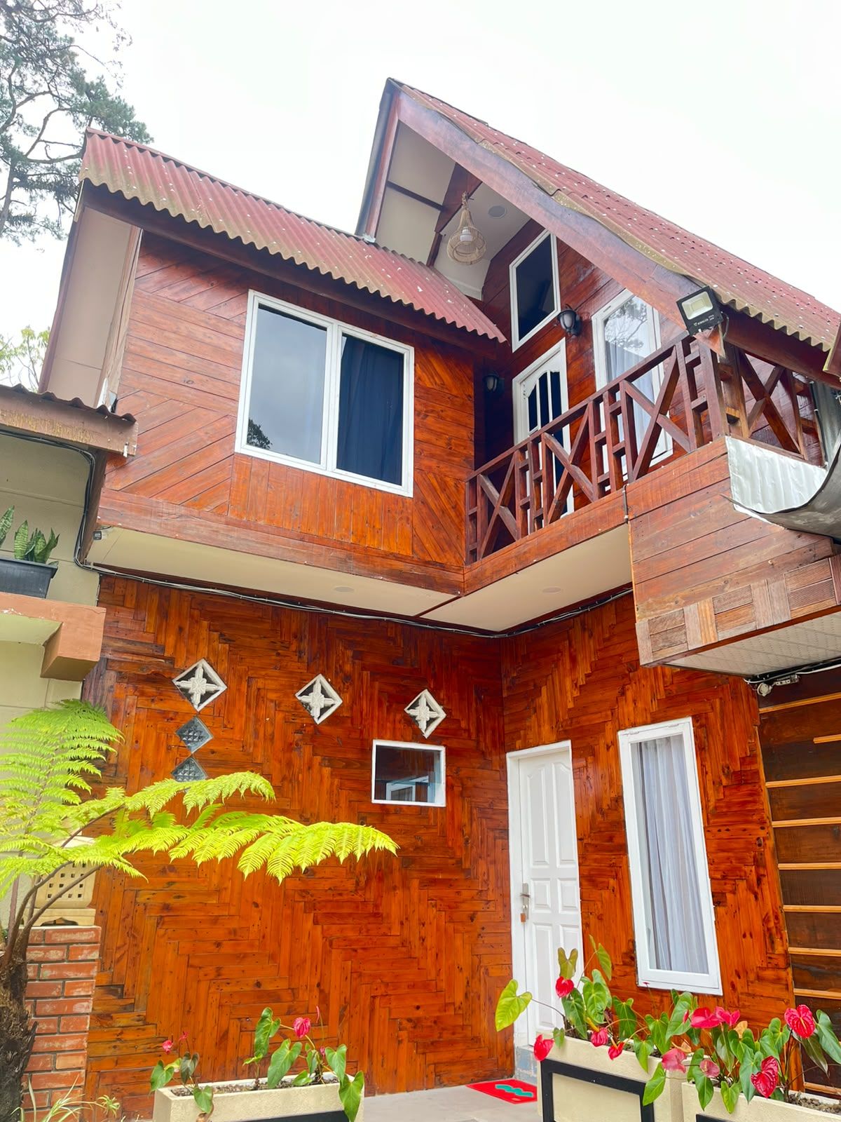 Una casa de madera de dos pisos con un balcón, un muro con patrón de espiga y una puerta con ventana.