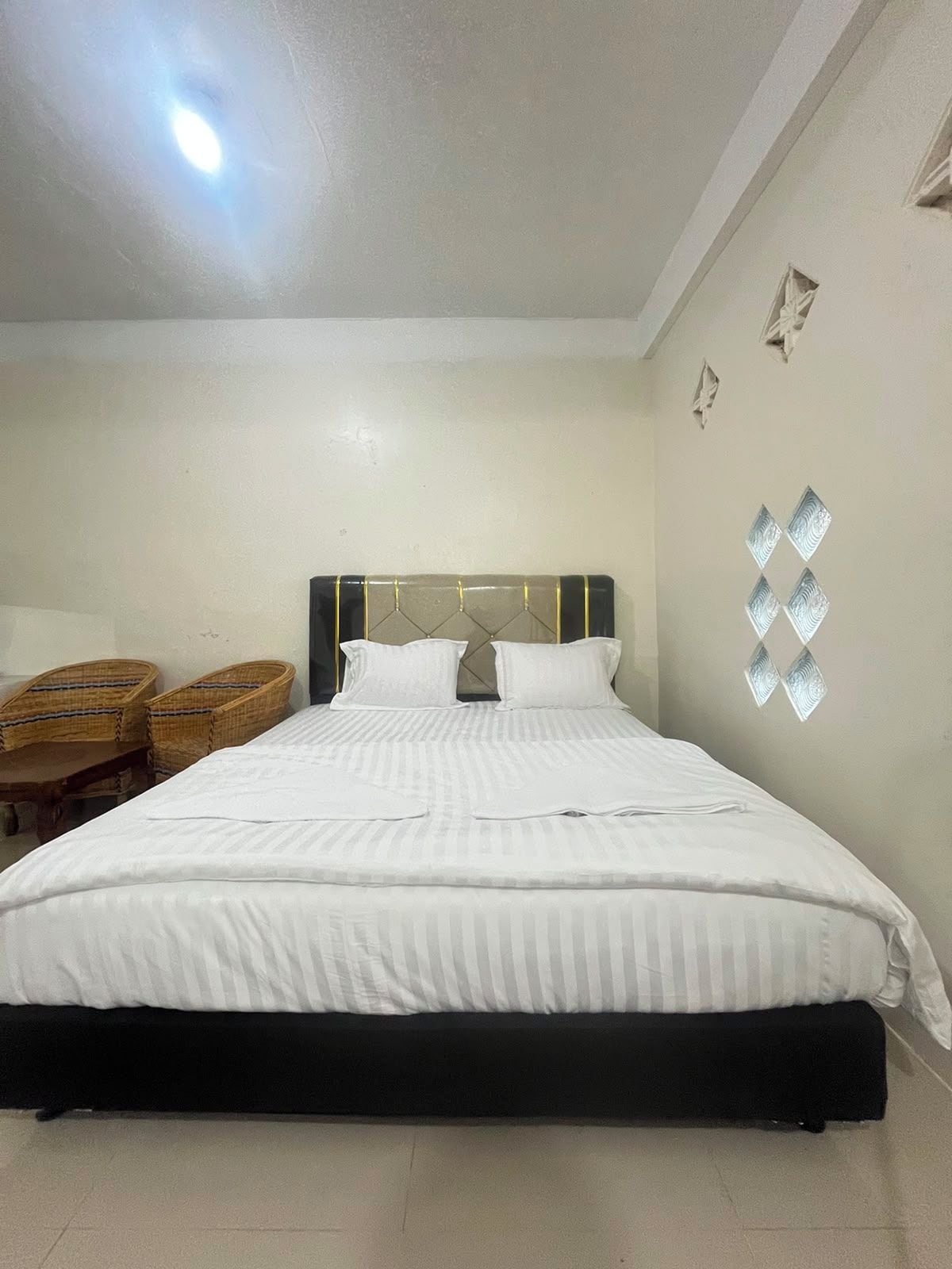 Un lit bien fait, avec une tête de lit, deux tables de chevet et un mur agrémenté d’appliques décoratives.