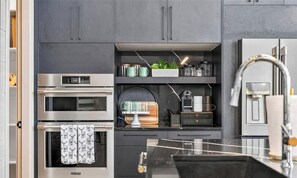 A modern kitchen with built-in appliances, a black countertop, and a stainless steel sink.