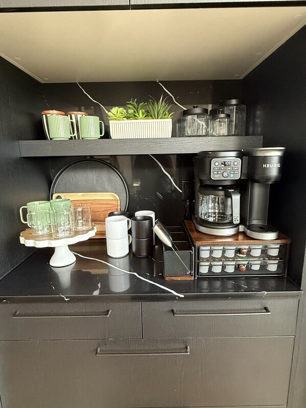 A kitchenette with a coffee maker, a kettle, a coffee grinder, and a small plant on the counter.