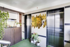 A modern elevator with a metallic finish, a wall-mounted decorative panel, and a small indoor garden with potted plants. - Townhouse Andheri Near Western Express (Mumbai)