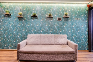 A room with a floral wallpaper, a beige sofa, and several hanging planters. - Townhouse Andheri Near Western Express (Mumbai)