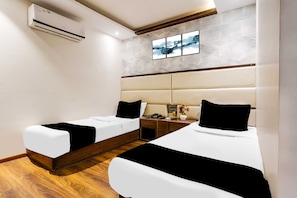 Habitación de hotel con dos camas, suelo de madera, aire acondicionado de pared, mesita de noche con teléfono y un cuadro sobre la cama.