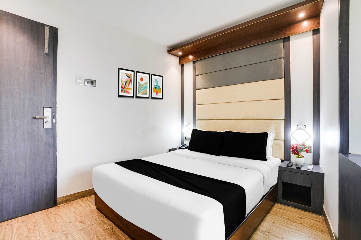 Una habitación de hotel con cama, mesita de noche, lámpara y una obra de arte en la pared.