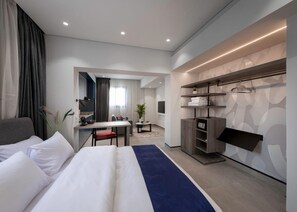 Ein modernes Hotelzimmer mit einem großen Bett, einem Schreibtisch, einer Sitzecke und einem Kleiderschrank mit Spiegel.