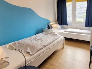 Une chambre avec un lit simple, une table de chevet, une lampe et une fenêtre avec des rideaux.