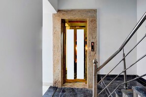 Un ascensor modern amb una porta daurada, una paret de marbre i una barana metàl·lica.