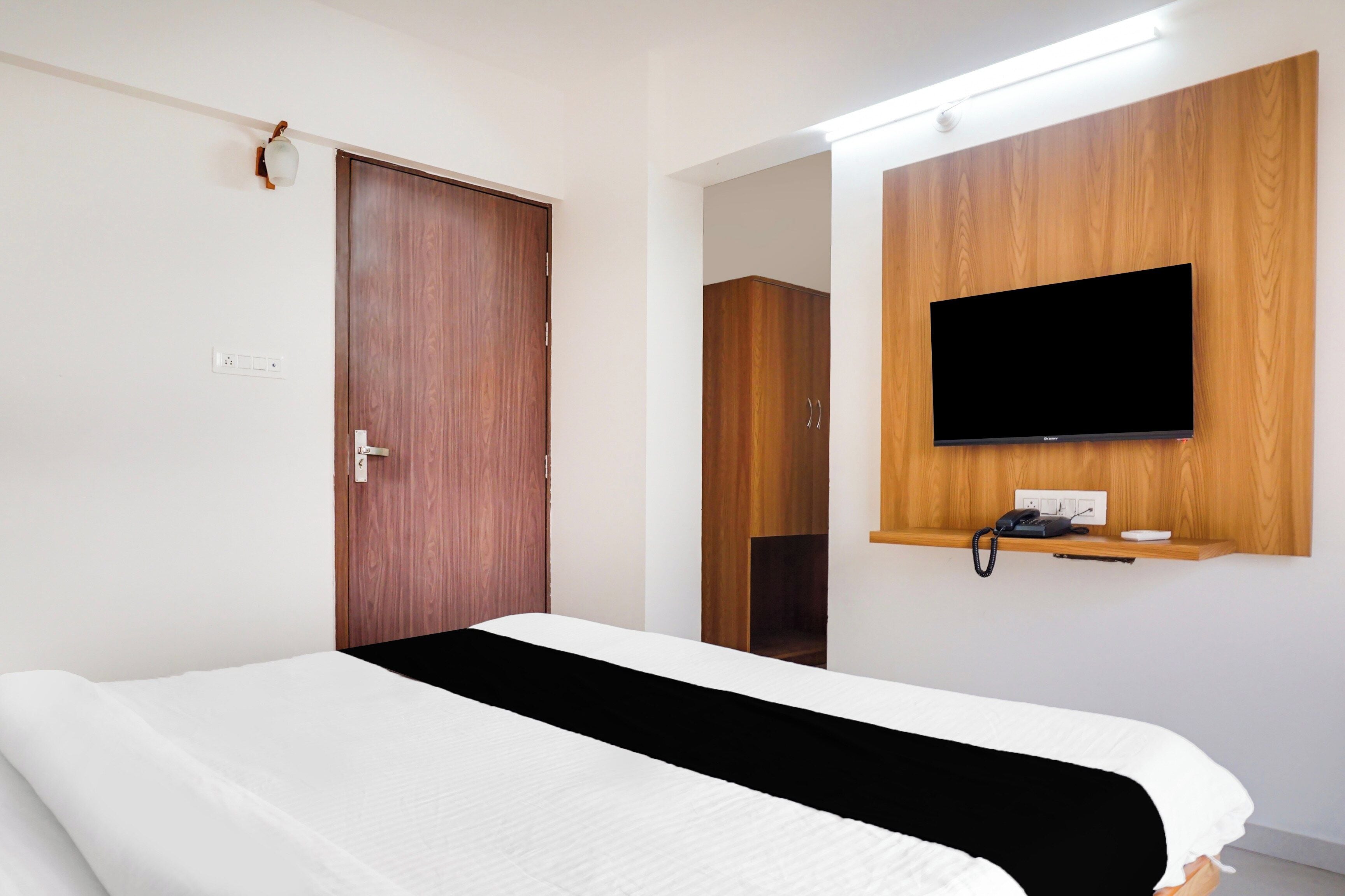 Una habitación de hotel con una cama, un armario de madera, un televisor montado y un teléfono.
