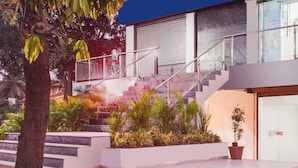 A modern building with a staircase leading to an upper level, surrounded by potted plants and a tree.
