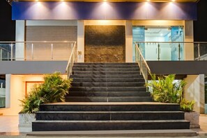 Un edificio moderno con una escalera que lleva a una entrada, rodeado de plantas en macetas.