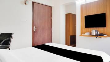 A hotel room with a bed, a television mounted on the wall, a coffee maker, and a chair.
