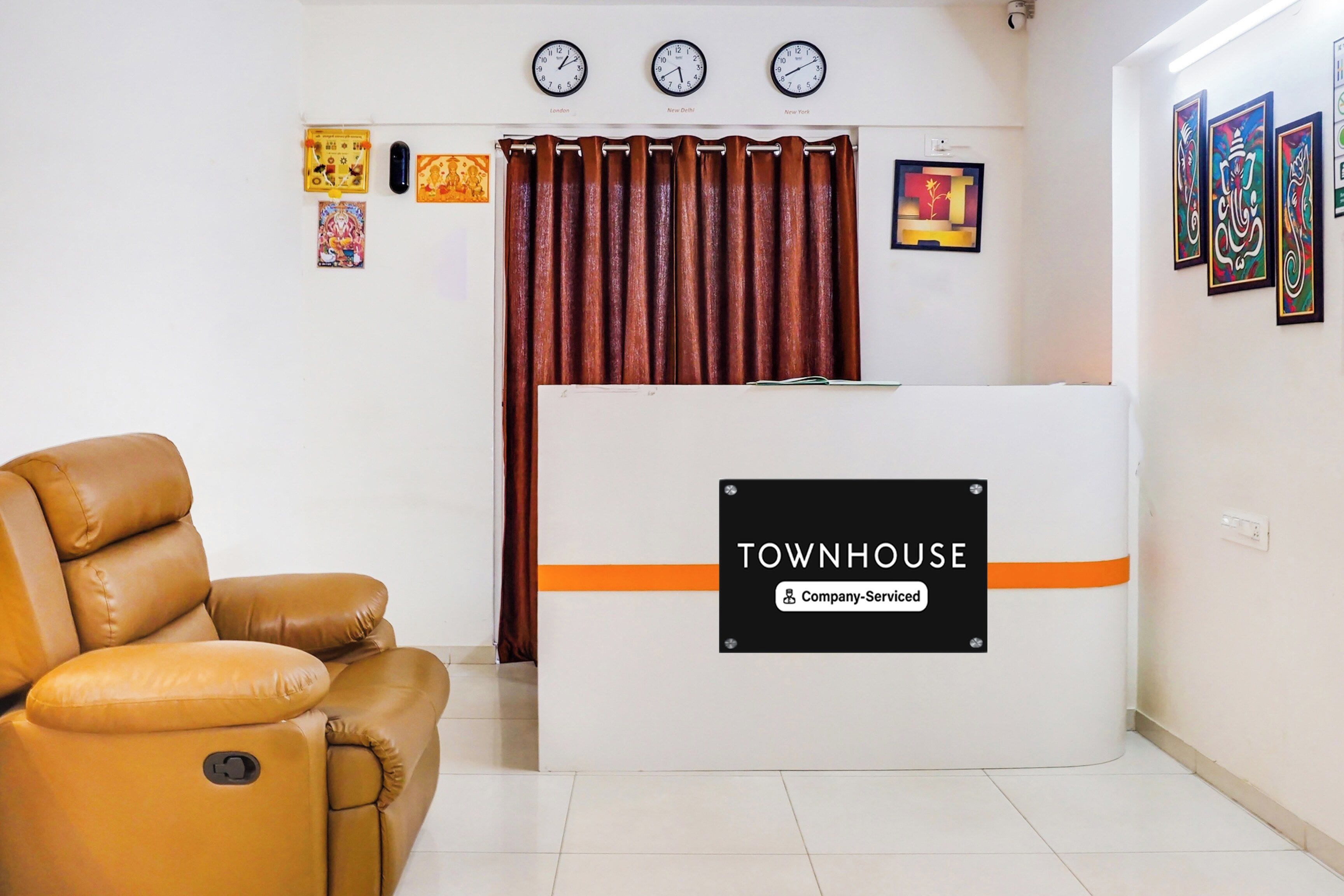 Ein Empfangsbereich mit Ledersessel, einer Rezeption mit der Aufschrift 'TOWNHOUSE Company-Serviced' und Uhren, die verschiedene Zeitzonen anzeigen.