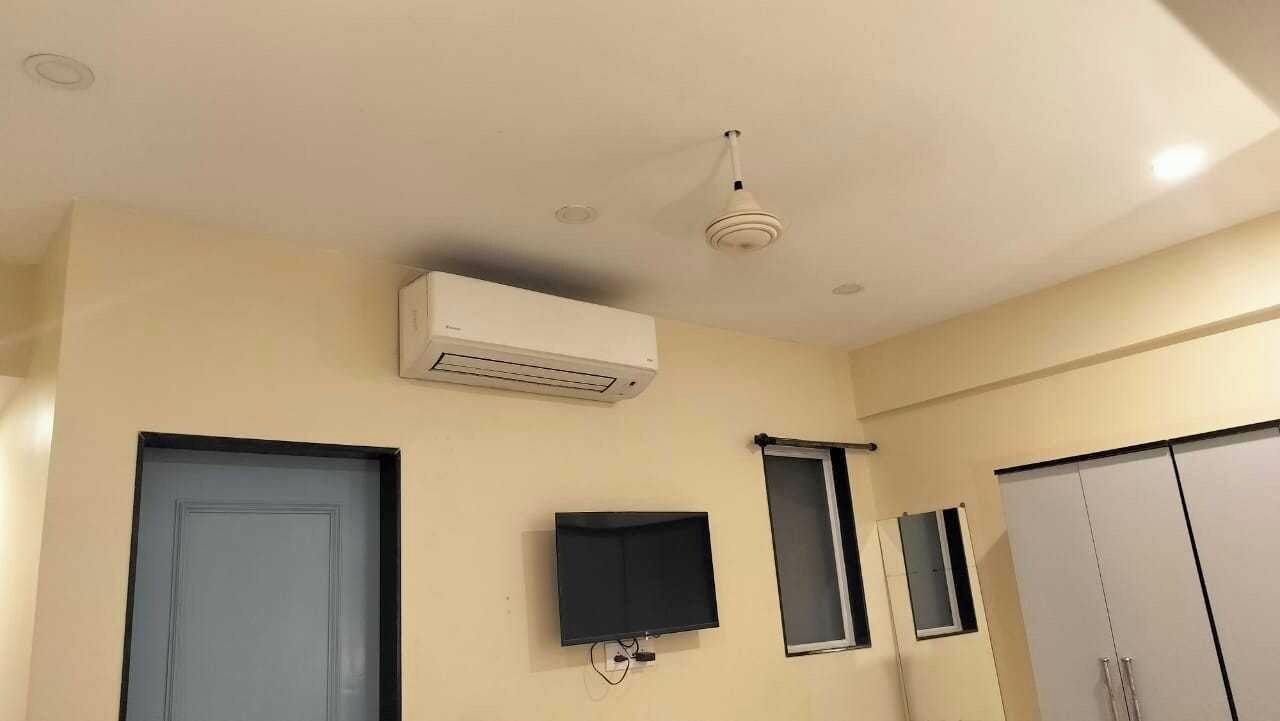 Una habitación con televisor de pantalla plana montado en la pared, aire acondicionado instalado en el techo, una puerta y un armario.
