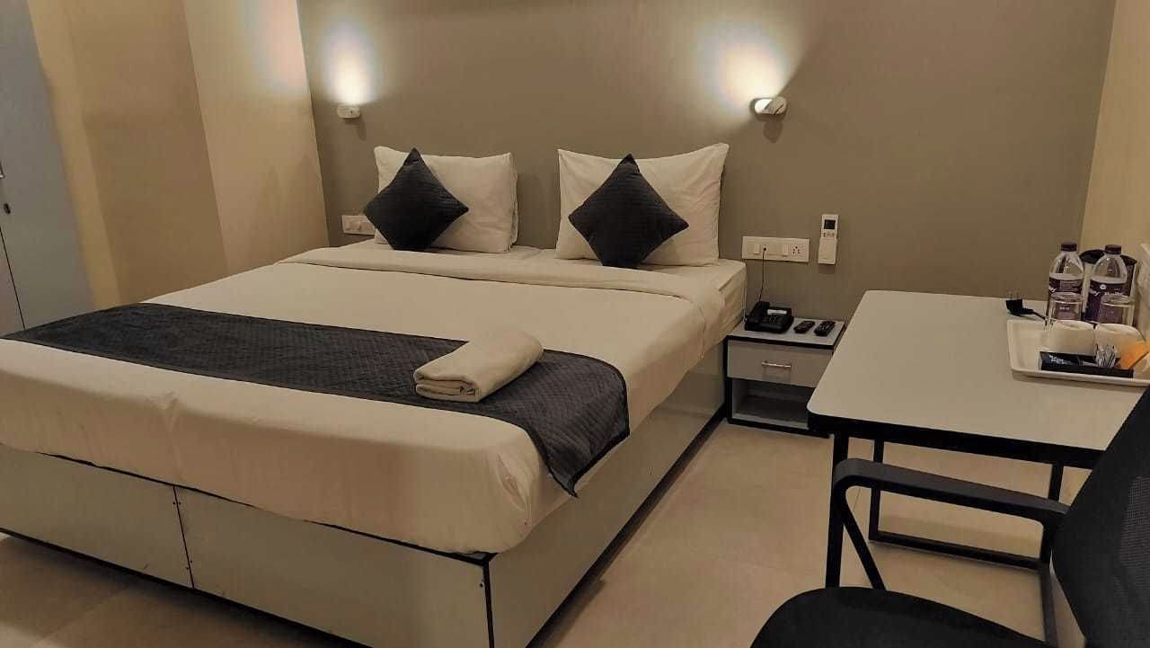 Una habitación de hotel con cama, mesita de noche, silla y una pequeña mesa con bandeja.