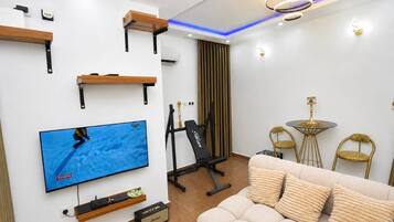 Un salon moderne équipé d’un téléviseur à écran plat, d’appareils de musculation, d’un canapé et d’une petite table ronde avec des chaises.