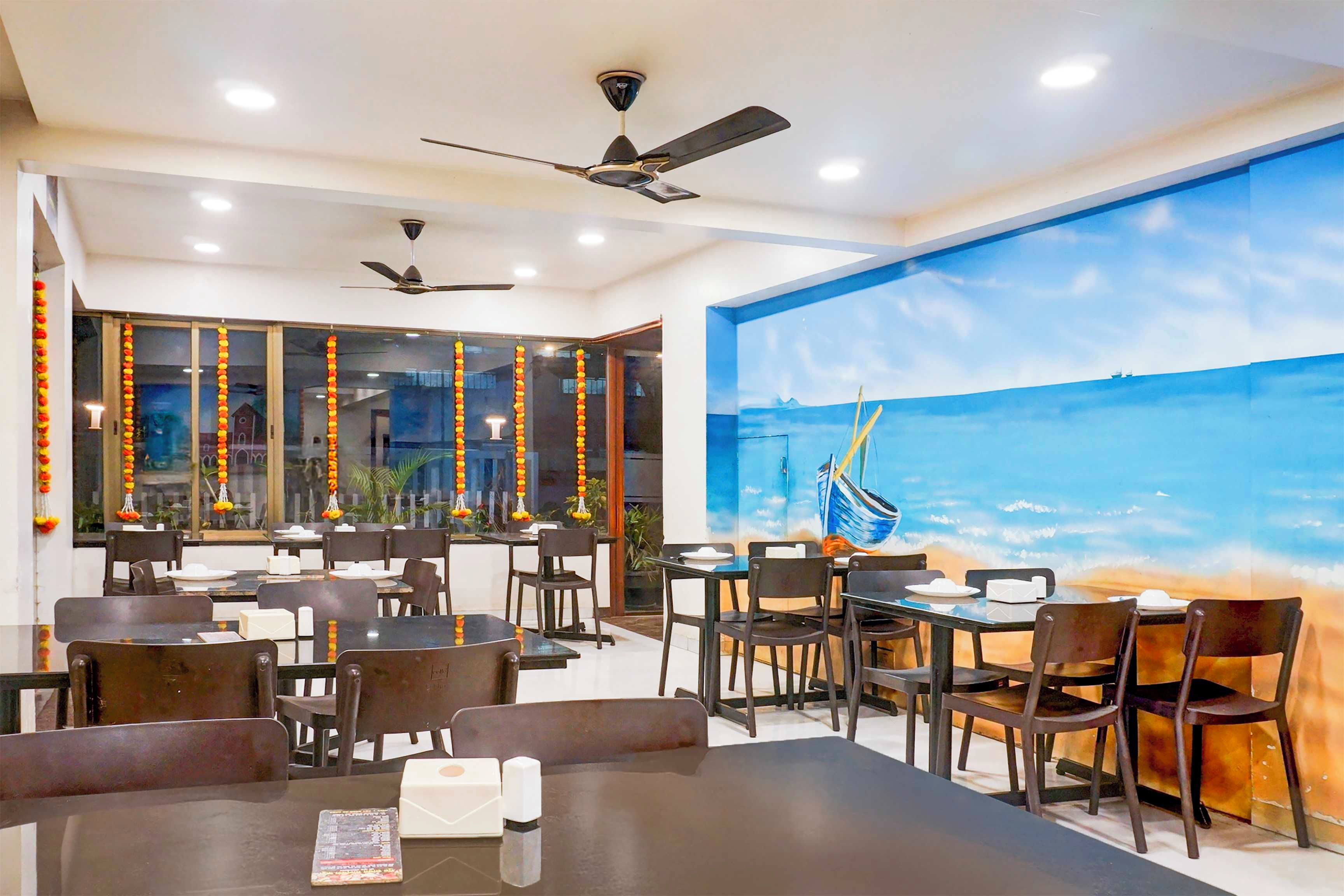 Un restaurant doté de nombreuses tables et chaises, de ventilateurs de plafond et d’une grande fresque murale représentant un voilier.