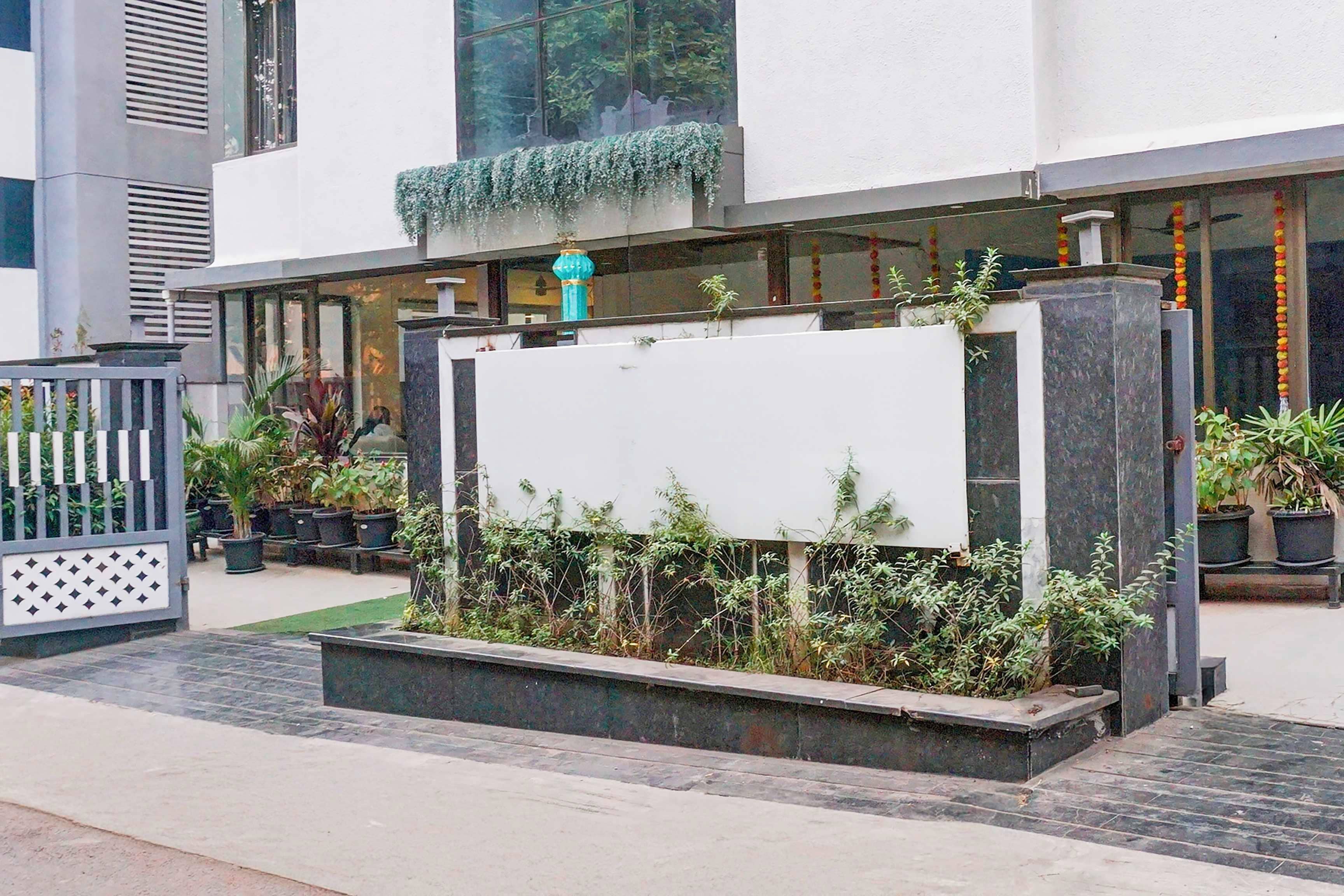 Ein Hotel Eingang mit einem großen, leeren Schild, Zimmerpflanzen und einem mit Fliesen belegten Weg zum Eingang.
