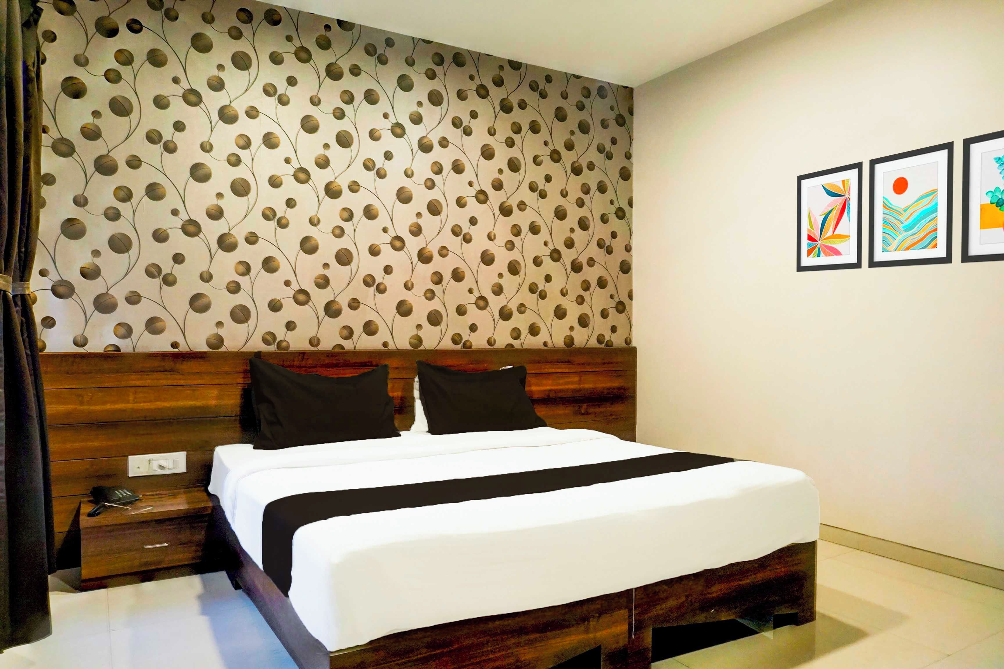 Ein Schlafzimmer mit einem hölzernen Kopfteil, einem Bett mit weißer Bettwäsche, zwei schwarzen Kissen, einem Nachttisch mit Telefon und einer Wand mit einem kreisförmigen Muster.