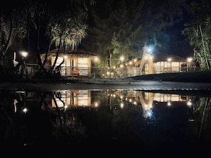 A nighttime scene with thatched-roof huts and string lights, reflecting on a calm water surface. - Ratnodwip Beach View Resort (Saint Martin's Island)