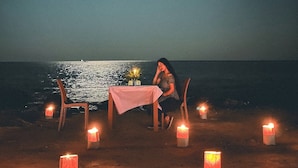 A person seated at a table with a pink tablecloth, surrounded by candles, at a beach at night. - Ratnodwip Beach View Resort (Cox's Bazar)