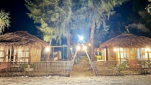 A night scene of a resort with thatched-roof huts, a central pathway, and a large tree. - Ratnodwip Beach View Resort (Cox's Bazar)