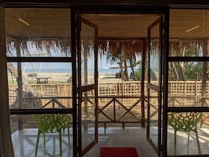 A beach view through a glass door with a wooden frame, a red mat, and green chairs. - Ratnodwip Beach View Resort (Saint Martin's Island)