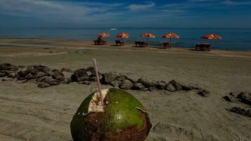 Escena de playa con un coco en la mano, cielo despejado y varias sombrillas de playa al fondo.