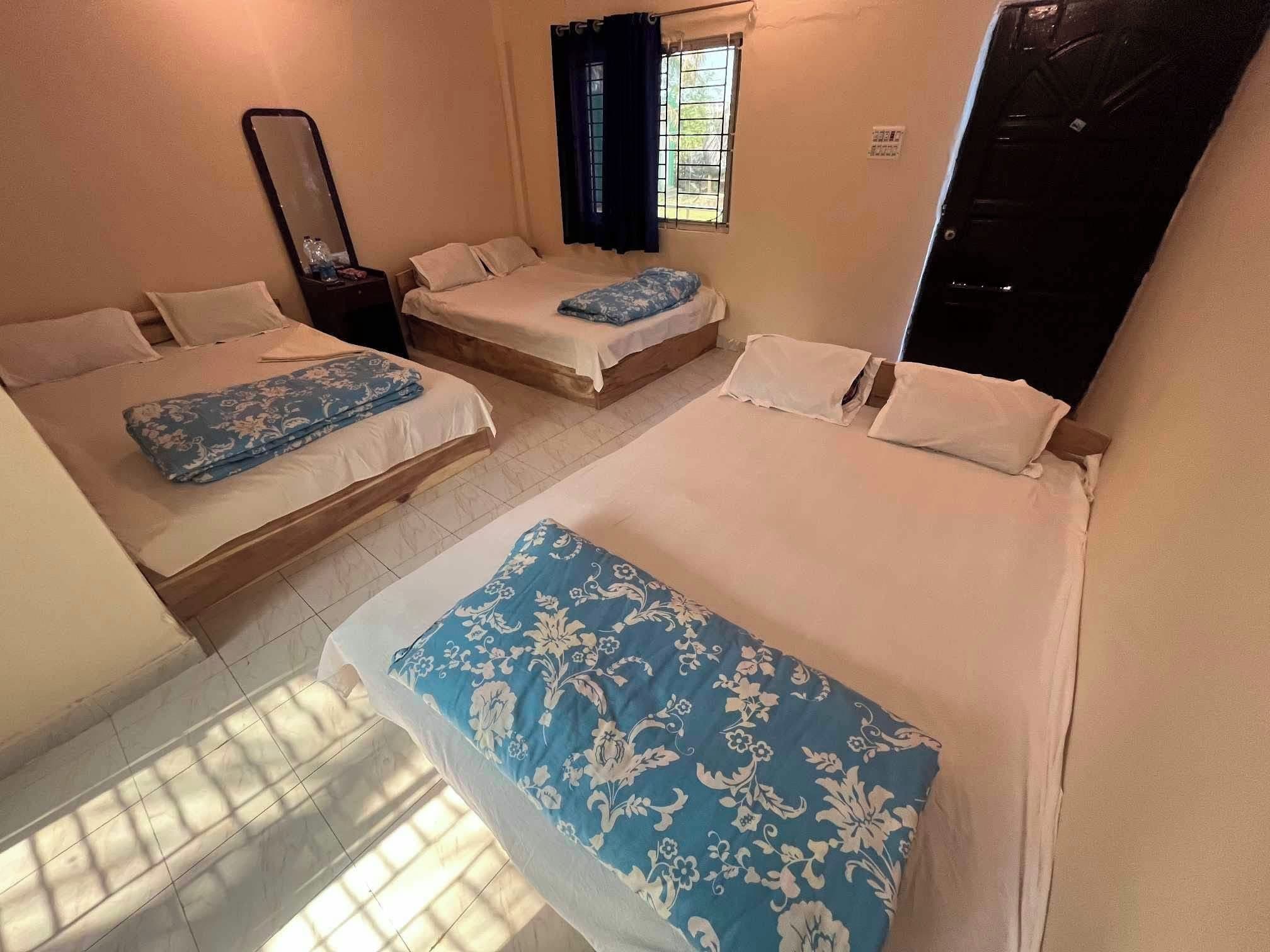 A room with three beds, a window with curtains, a mirror, and a door.