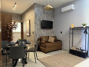 A modern living room with a sofa, a dining table set with plates and cups, a flat-screen TV mounted on the wall, and a potted plant. - Near the beach with a rooftop pool – By GPSRentas (Mazatlán)