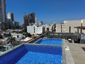 A rooftop pool with clear blue water, surrounded by modern buildings and palm trees. - Near the beach with a rooftop pool – By GPSRentas (Mazatlán)