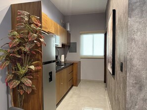 A compact kitchen with wooden cabinets, a built-in refrigerator, and a window providing natural light. - Near the beach with a rooftop pool – By GPSRentas (Mazatlán)