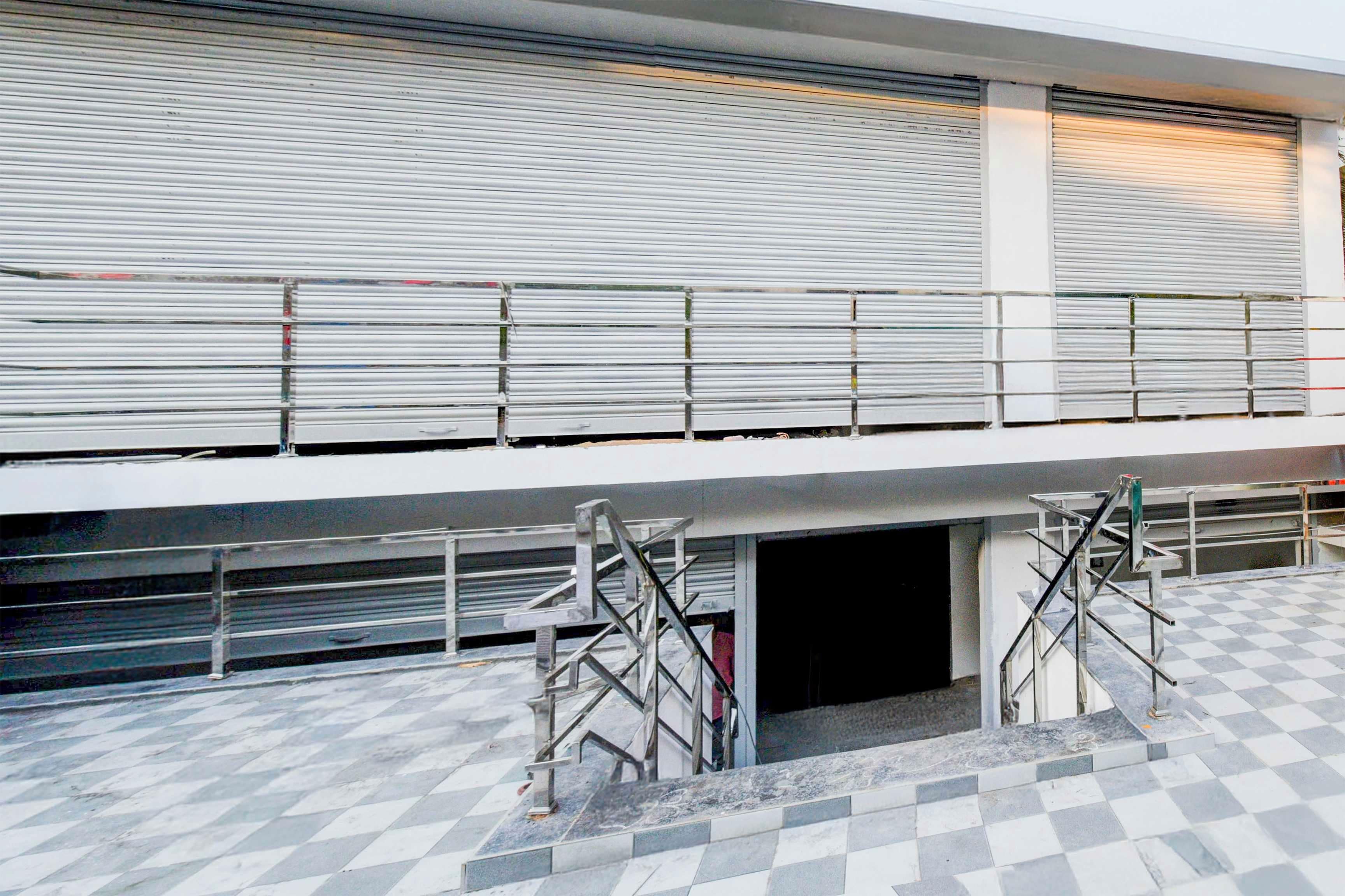 A building with a closed shuttered entrance, metal scaffolding, and a checkered floor pattern.