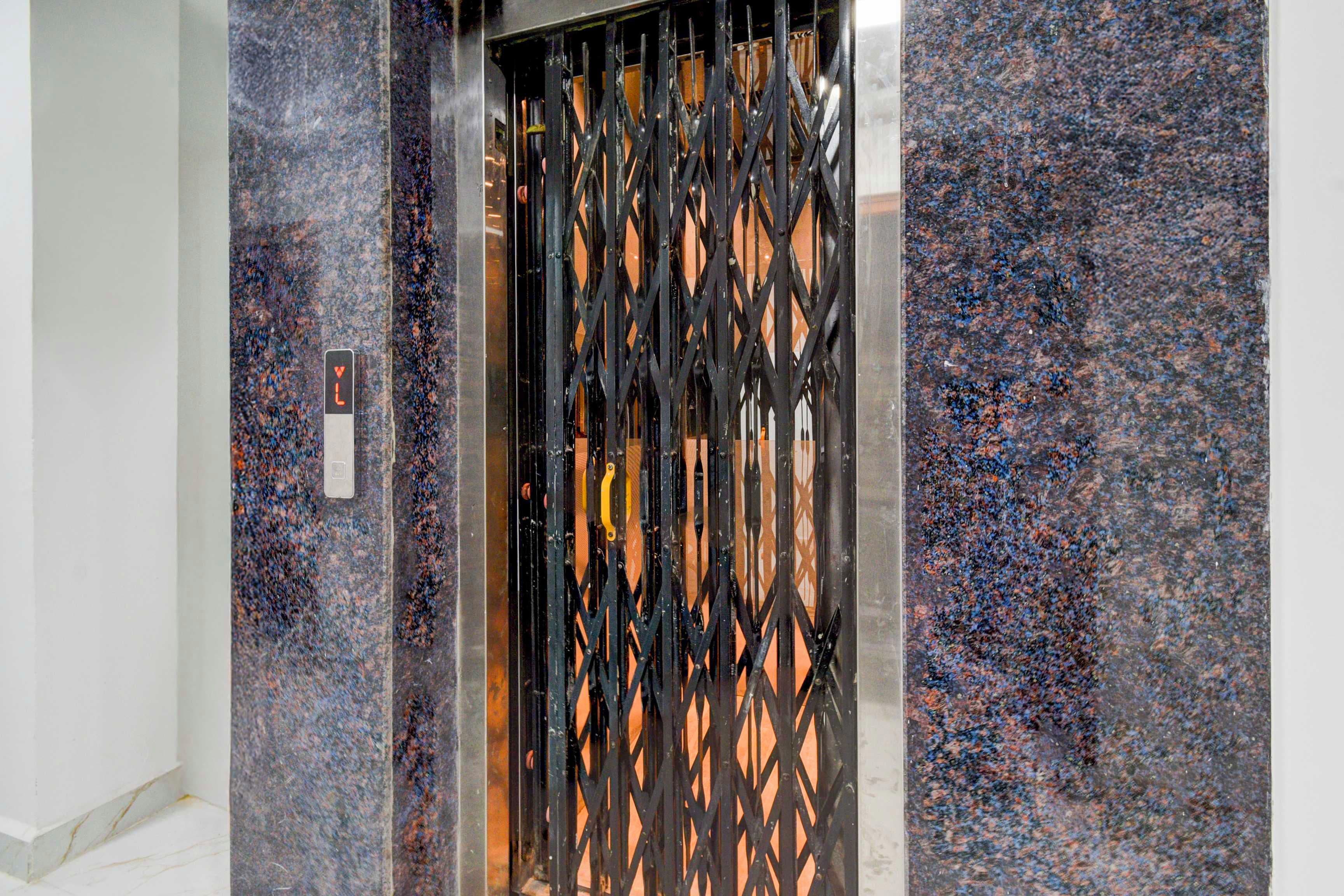 An elevator with a black metal gate and a marble wall.