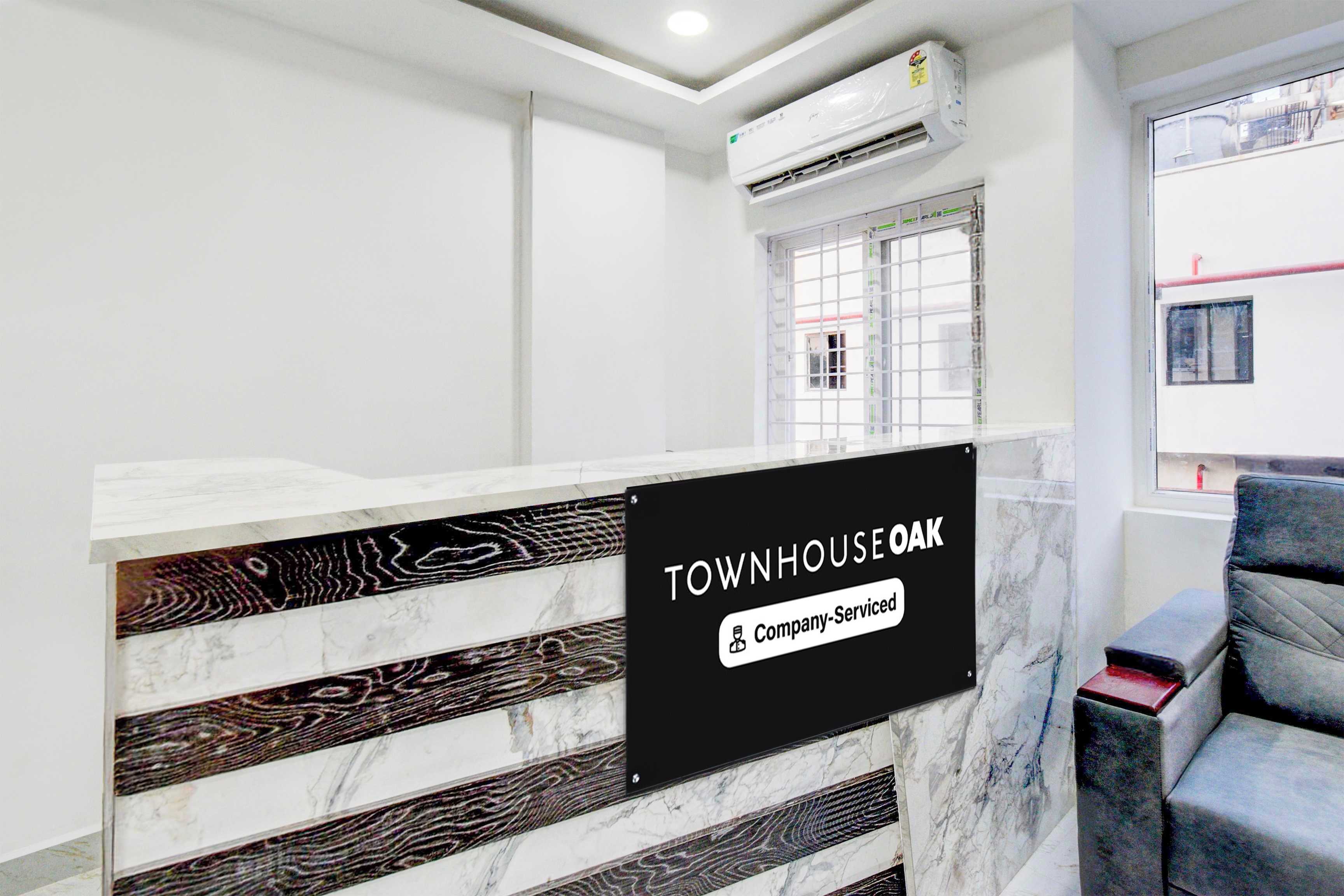 A reception desk with a marble design, a sign indicating 'TOWNHOUSE OAK & Company-Serviced', and a window with a view of the outside.