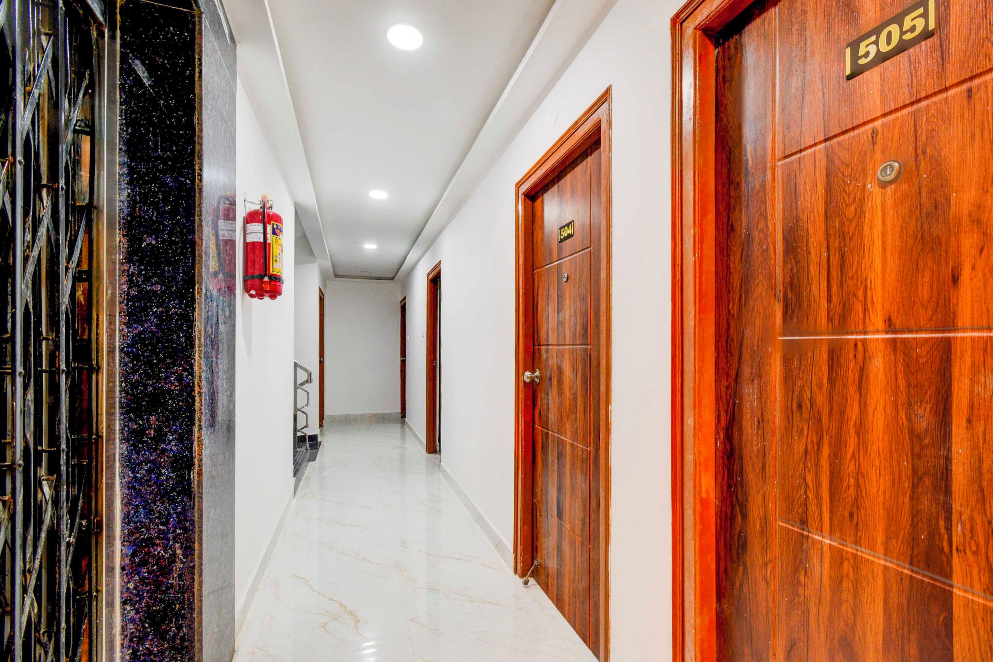 Un pasillo de hotel con puertas de madera, un extintor y piso de mármol.