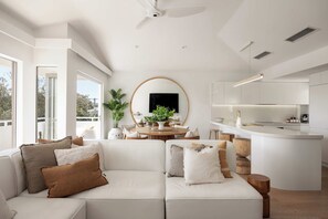 A modern living room with a white sofa, a dining table, and a kitchen area. - Boutique Top-Floor Riverfront Apartment (Noosaville)
