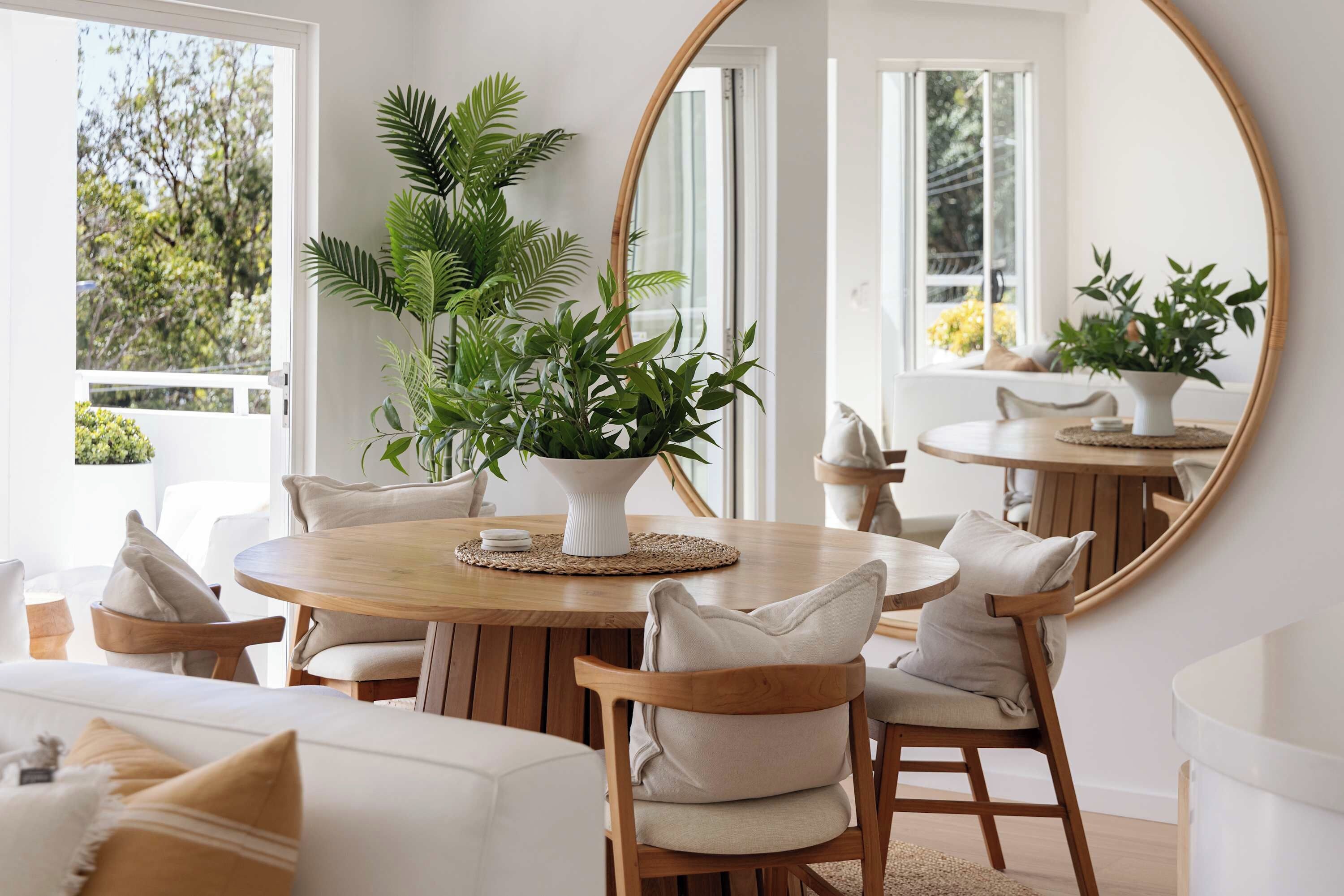 A dining area with a round wooden table, white chairs, and a large mirror on the wall.