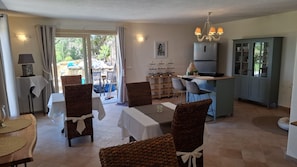 Un comedor con sillas de mimbre y una mesa, una cocina con refrigerador, y vistas al exterior.