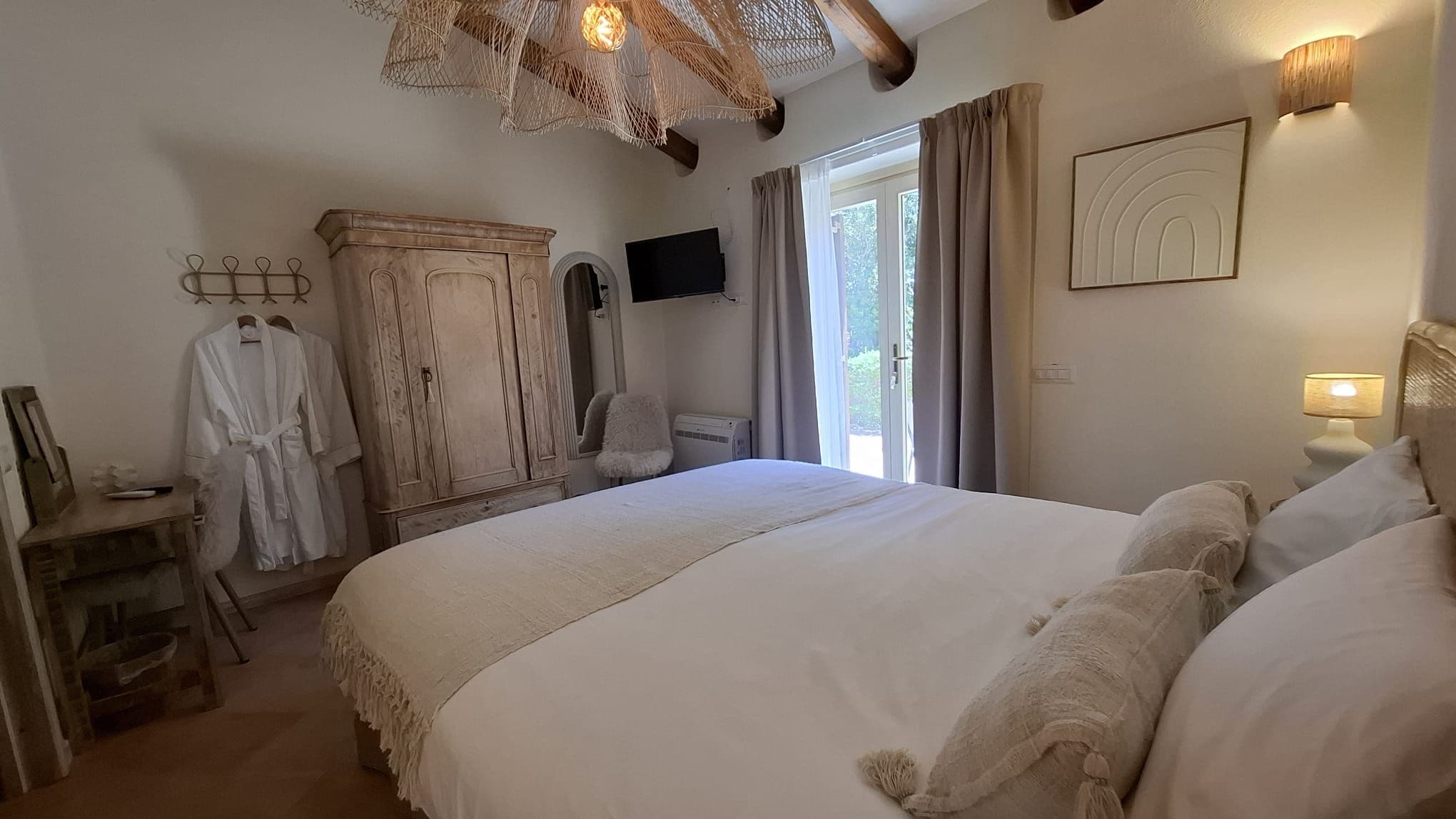 Un dormitorio con una cama grande, un armario, una silla, un televisor y una ventana con cortinas.