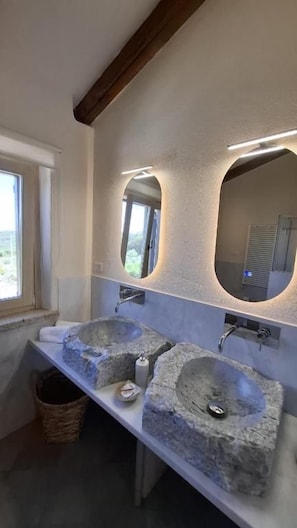 A bathroom with two stone sinks, a window, and a mirror with integrated lighting. - Stazzu La Vigna di Maria (Luogosanto)