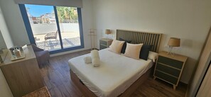 Ein Schlafzimmer mit einem Bett, Nachttischen, einem Schreibtisch und Blick ins Freie.