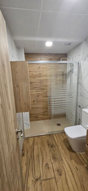 Ein Badezimmer mit Holzboden, einer Duschkabine aus Glas, einer Toilette und einem Holzschrank.