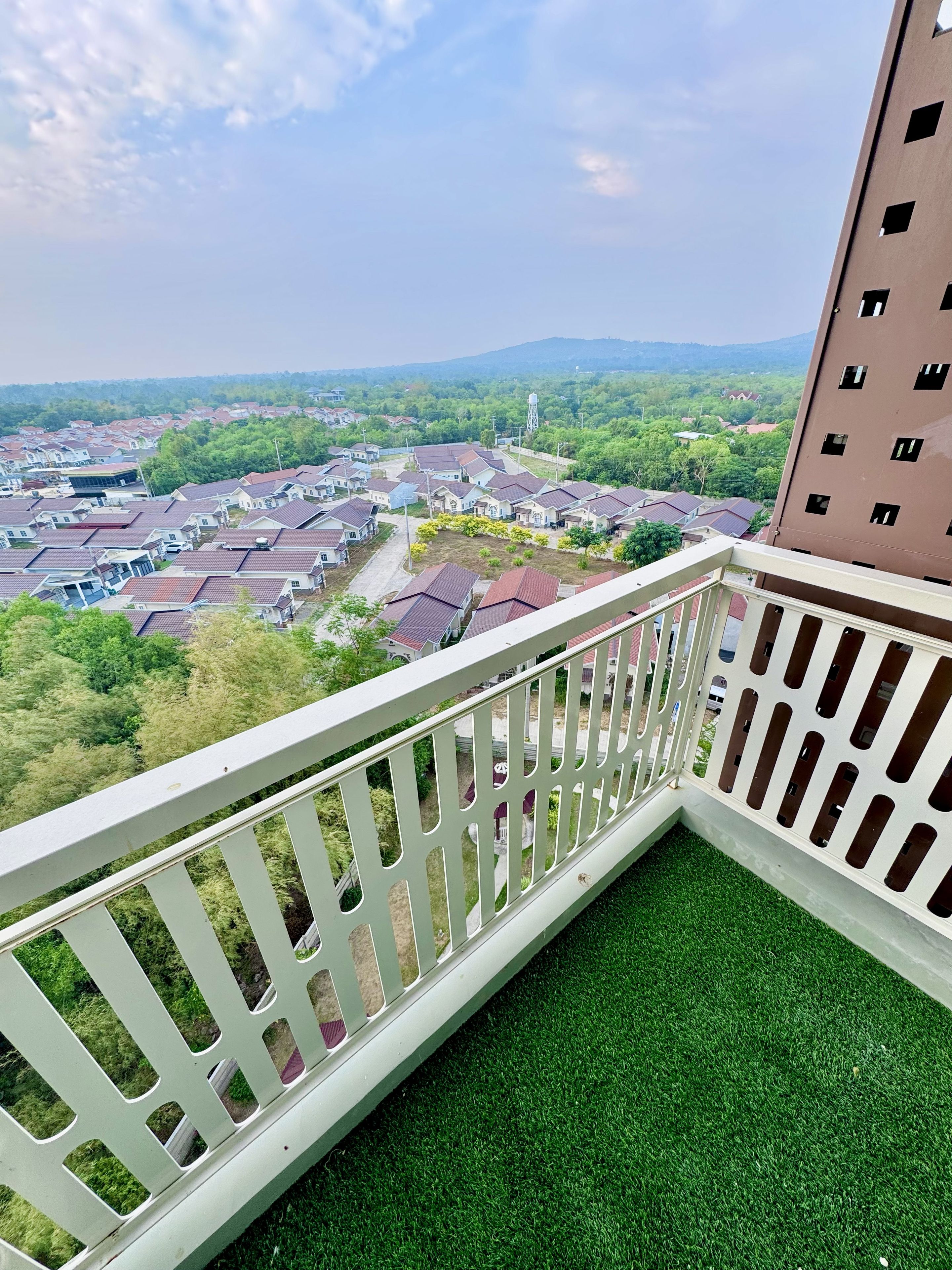 Ein Balkon mit weißer Reling, der auf ein Wohngebiet mit Häusern und Grünflächen blickt.