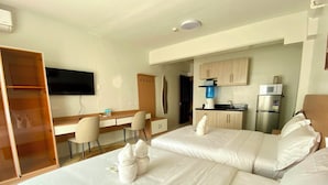 Hotellihuone, jossa on kaksi sänkyä, työpöytä, tuoli, televisio ja pieni keittiönurkkaus.