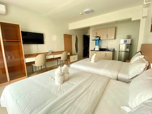 A hotel room with two beds, a desk, a chair, a TV, and a kitchenette. - Royal Oceancrest Panglao 1 (Dauis)