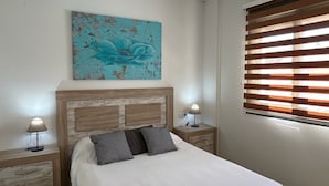Ein Schlafzimmer mit einem Bett, zwei Nachttischen, einem Wandbild, einem Fenster mit Jalousien und einer Deckenleuchte.